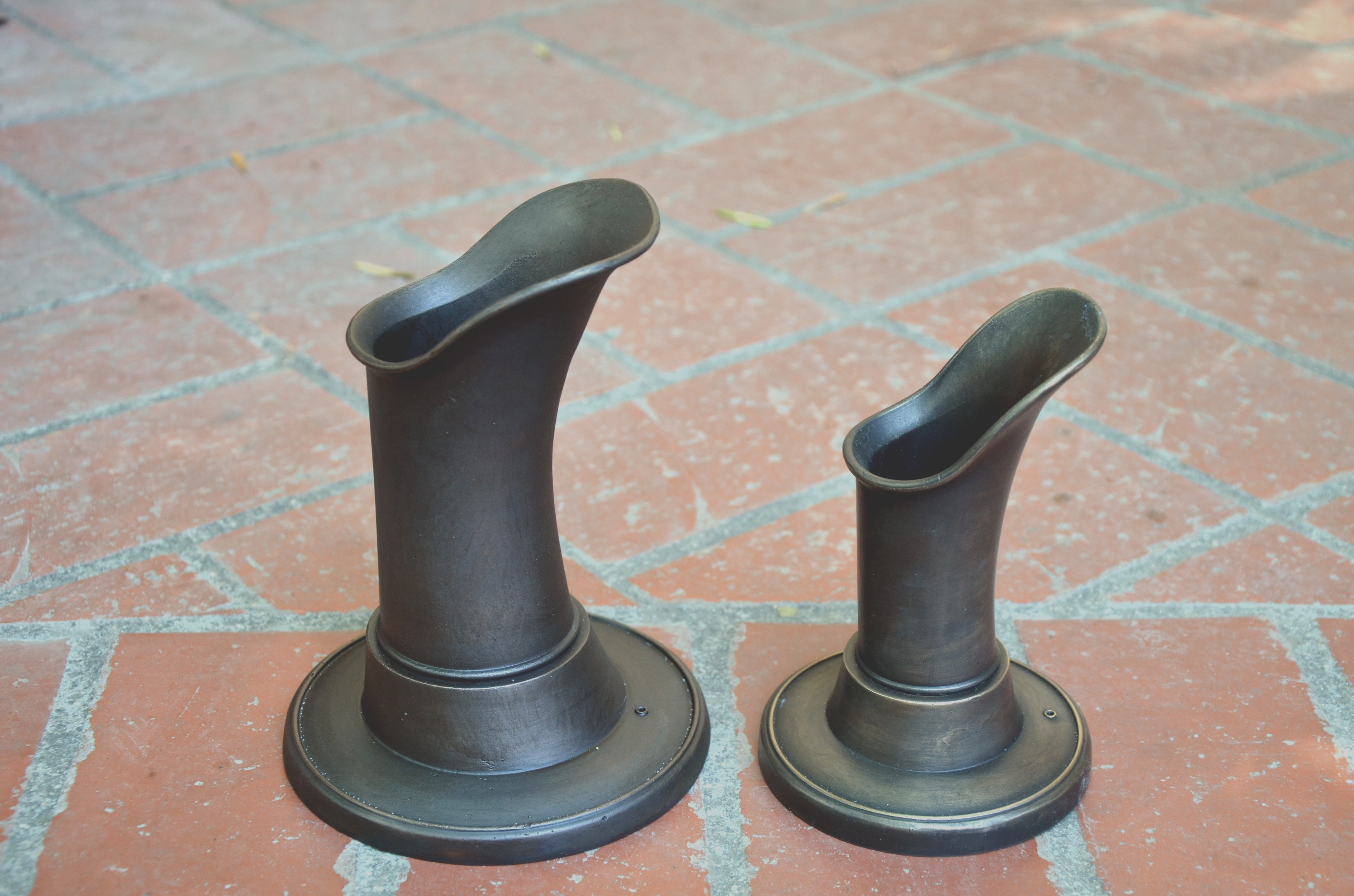 A small, medium and large sized fountain spout on a brick floor